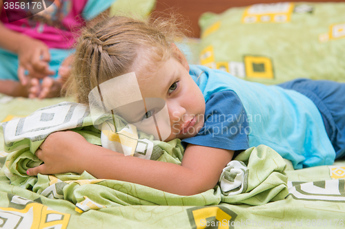 Image of Little girl sitting on a double bed and frightened looks into the distance