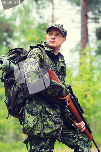 Image of young soldier or hunter with gun in forest
