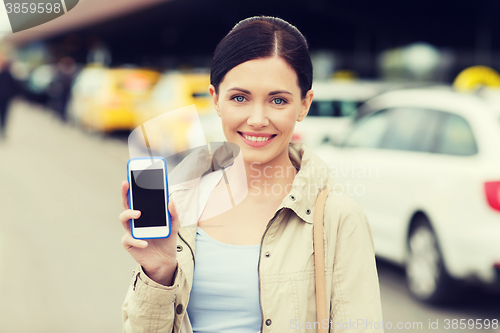 Image of smiling woman showing smartphone over taxi in city