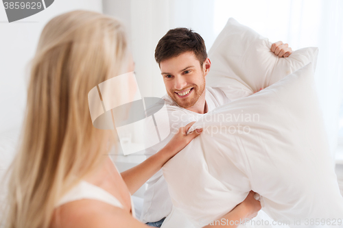 Image of happy couple having pillow fight in bed at home