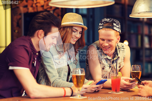 Image of happy friends with smartphones and drinks at bar