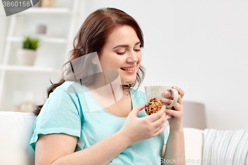 Image of happy plus size woman with cup and cookie at home