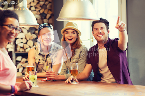 Image of happy friends with drinks pointing finger at bar