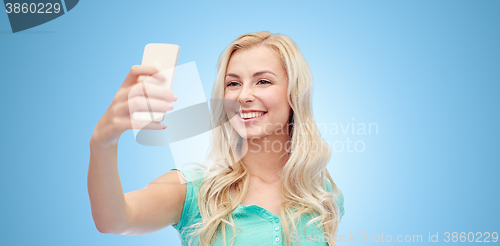 Image of smiling young woman taking selfie with smartphone