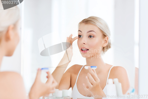 Image of young woman putting on contact lenses at bathroom