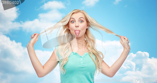 Image of happy young woman showing tongue and holding hair