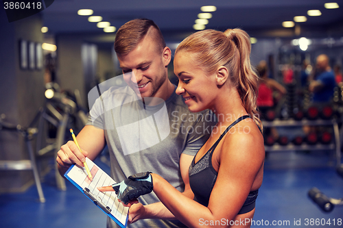 Image of smiling woman with trainer and clipboard in gym