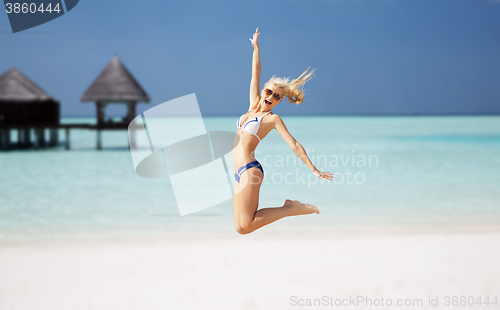 Image of happy young woman jumping over exotic beach