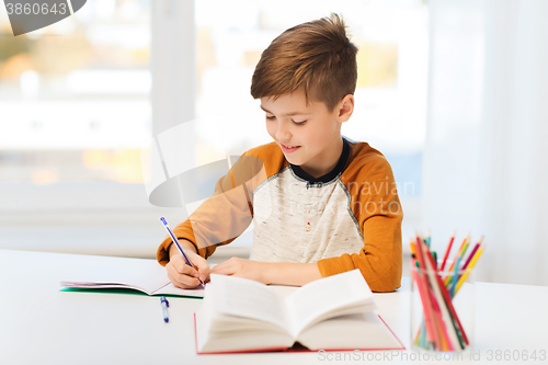 Image of smiling student boy writing to notebook at home