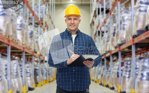 Image of happy man in helmet with clipboard at warehouse