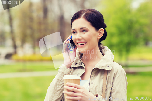 Image of smiling woman with smartphone and coffee in park