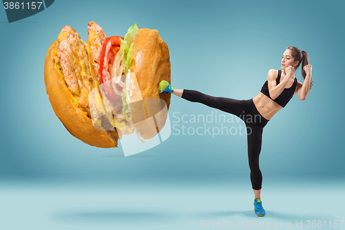 Image of Fit, young, energetic woman boxing hamburger as unhealthy food