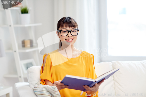 Image of smiling young asian woman reading book at home