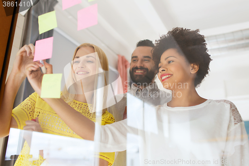 Image of happy creative team writing on stickers at office