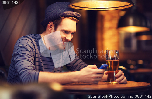 Image of man with smartphone and beer texting at bar