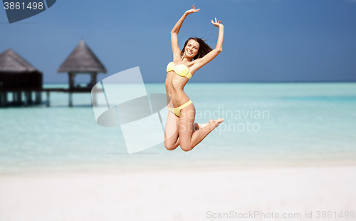 Image of happy young woman jumping over exotic beach