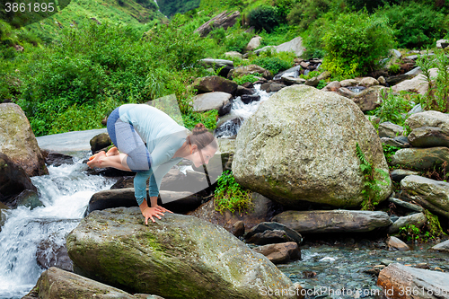 Image of Woman doing Kakasana asana arm balance outdoors