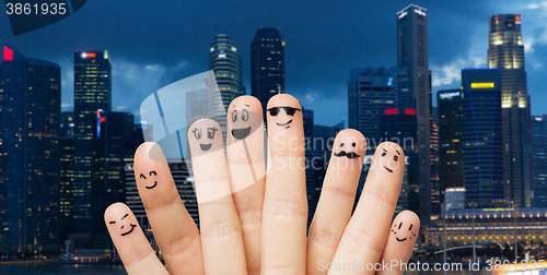 Image of close up of fingers with smiley faces over city