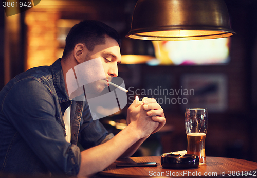 Image of man drinking beer and smoking cigarette at bar