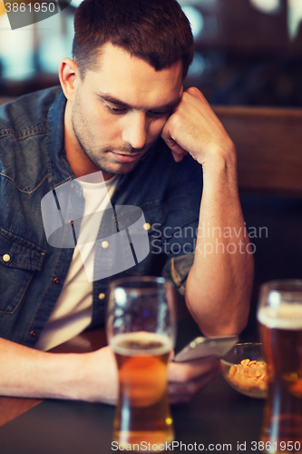 Image of man with smartphone drinking beer at bar