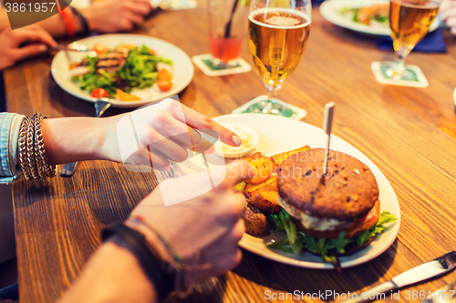 Image of close up of friends hands sharing burger at bar