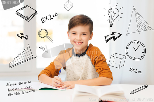 Image of smiling student boy writing to notebook at home