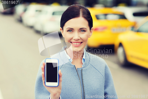 Image of smiling woman showing smartphone over taxi in city