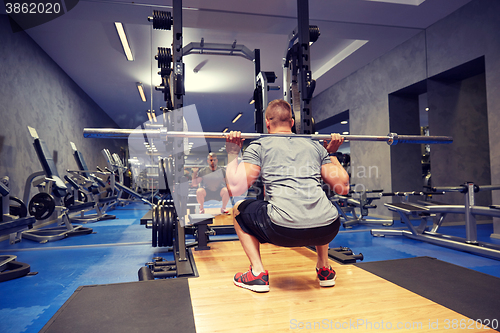 Image of young man flexing muscles with bar in gym