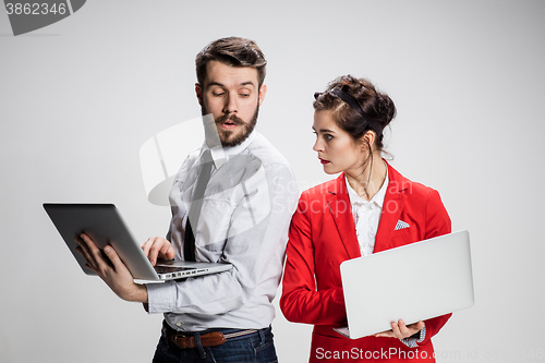 Image of The young businessman and businesswoman with laptops  communicating on gray background