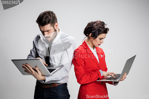 Image of The young businessman and businesswoman with laptops  communicating on gray background