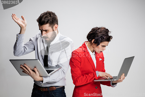 Image of The young businessman and businesswoman with laptops  communicating on gray background