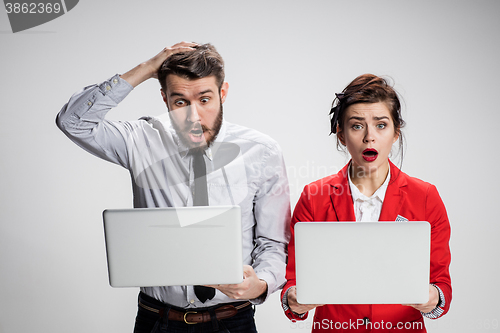 Image of The young businessman and businesswoman with laptops  communicating on gray background