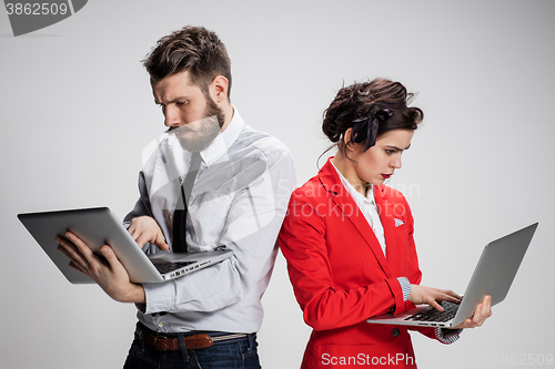 Image of The young businessman and businesswoman with laptops  communicating on gray background