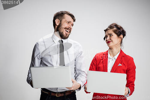 Image of The young businessman and businesswoman with laptops  communicating on gray background