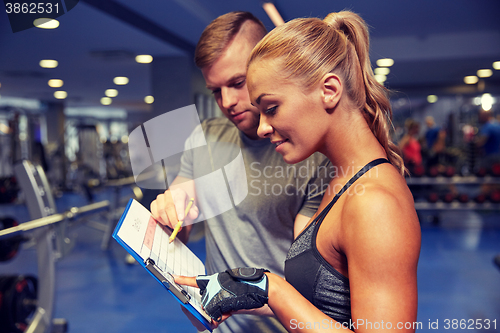 Image of smiling woman with trainer and clipboard in gym