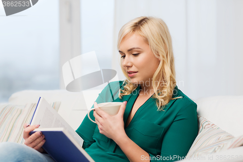 Image of  young woman with tea cup reading book at home