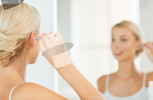 Image of woman cleaning ear with cotton swab at bathroom