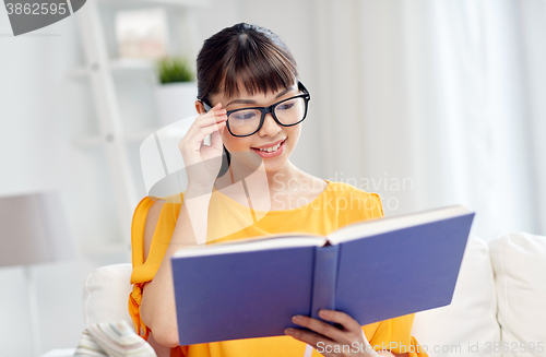 Image of smiling young asian woman reading book at home