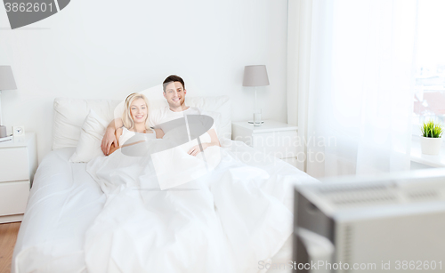 Image of happy couple lying in bed at home and watching tv