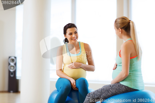 Image of two happy pregnant women sitting on balls in gym