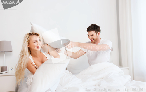 Image of happy couple having pillow fight in bed at home