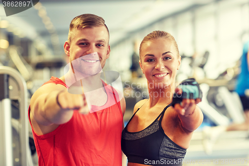 Image of happy man and woman pointing finger to you in gym