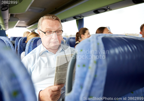 Image of happy senior man reading newspaper in travel bus