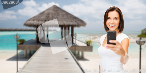 Image of happy woman taking picture by smartphone on beach