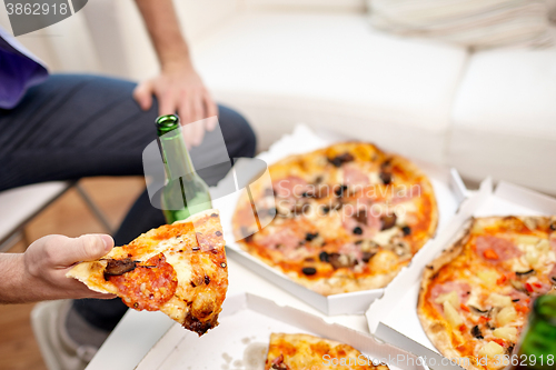 Image of close up of man eating pizza with beer at home