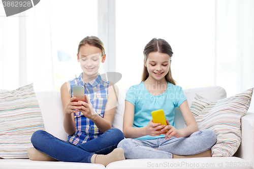 Image of happy girls with smartphones sitting on sofa