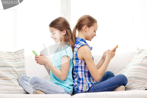 Image of happy girls with smartphones sitting on sofa