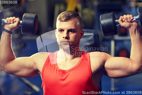 Image of young man with dumbbells flexing muscles in gym