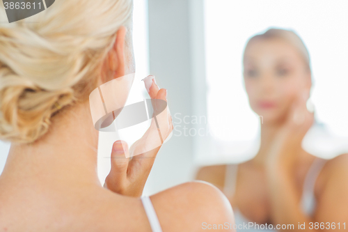 Image of close up of woman applying face cream at bathroom