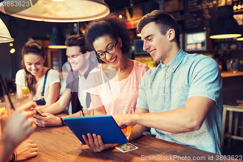 Image of happy friends with tablet pc and drinks at bar